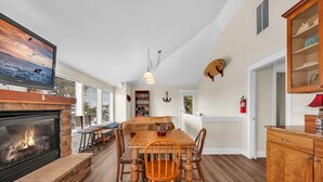 A dining area with a wooden table and chairs, a fireplace, a television, and a bookshelf. - Pacific City Oasis: Ocean Views, Game Room & Walk to Bob Straub Park (Pacific City)
