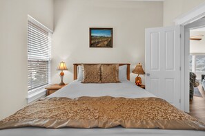 Een slaapkamer met een bed, twee bedlampen, een lijst aan de muur en een deur naar een andere kamer.