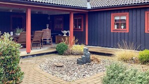 A house with a covered porch, a stone fountain, and a garden with various plants. - 4 Star Holiday Home in Eldsberga (Eldsberga)