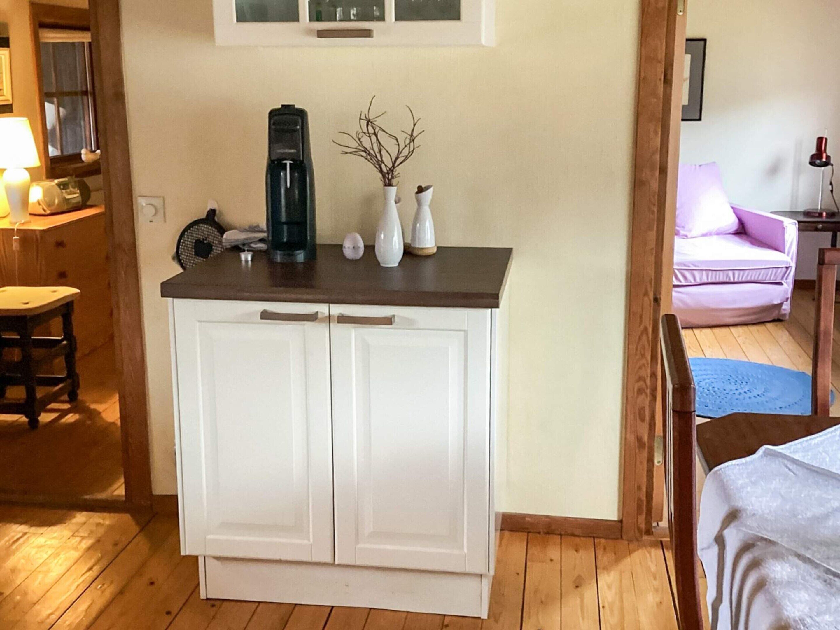 A small kitchenette with a coffee maker, a vase with branches, and a white cabinet.