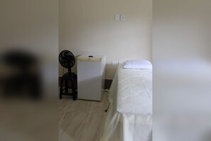 Una habitación pequeña y sencilla con cama, escritorio y ventilador.