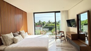 Een moderne hotelkamer met een groot bed, een televisie, een balkon met buitenmeubilair en uitzicht op groen.