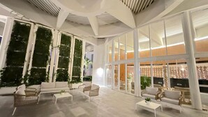 Een ruime lobby met hoge plafonds, grote ramen en kamerplanten.