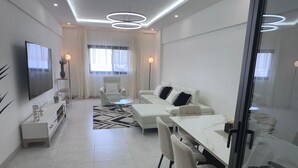 Un salon moderne comprenant un canapé, une table basse en verre, un téléviseur et un coin repas avec des chaises et une table.