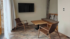 Une pièce dotée d’un téléviseur à écran plat, de deux fauteuils en osier, d’une table en bois, d’un canapé avec des coussins à motifs et d’un mur en pierre.