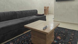 Un salon avec un canapé gris foncé, une table basse en bois sur laquelle se trouve une télécommande, un tapis à motifs et un téléviseur à écran plat fixé au mur.