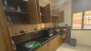 Une cuisine avec des meubles en bois, un plan de travail noir, un évier, une poubelle et une fenêtre donnant sur l’extérieur.