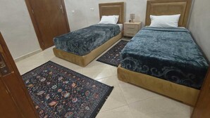 Une chambre avec deux lits, une porte en bois, une table de chevet et un tapis à motifs.