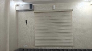 Une pièce dotée d’un climatiseur fixé au plafond, d’un thermostat mural et d’une fenêtre avec des stores horizontaux.
