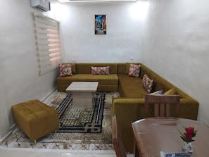 Ein Wohnzimmer mit einer Couch, Hocker, Couchtisch und einem gemusterten Teppich.