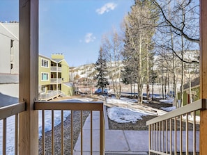 Vista desde un balcón sobre una zona residencial con un edificio de varios pisos, árboles y suelo cubierto de nieve.