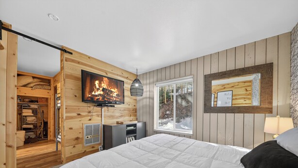 Ein Schlafzimmer mit Bett, einem an der Wand montierten Fernseher, einem Fenster und einem Holzschrank.