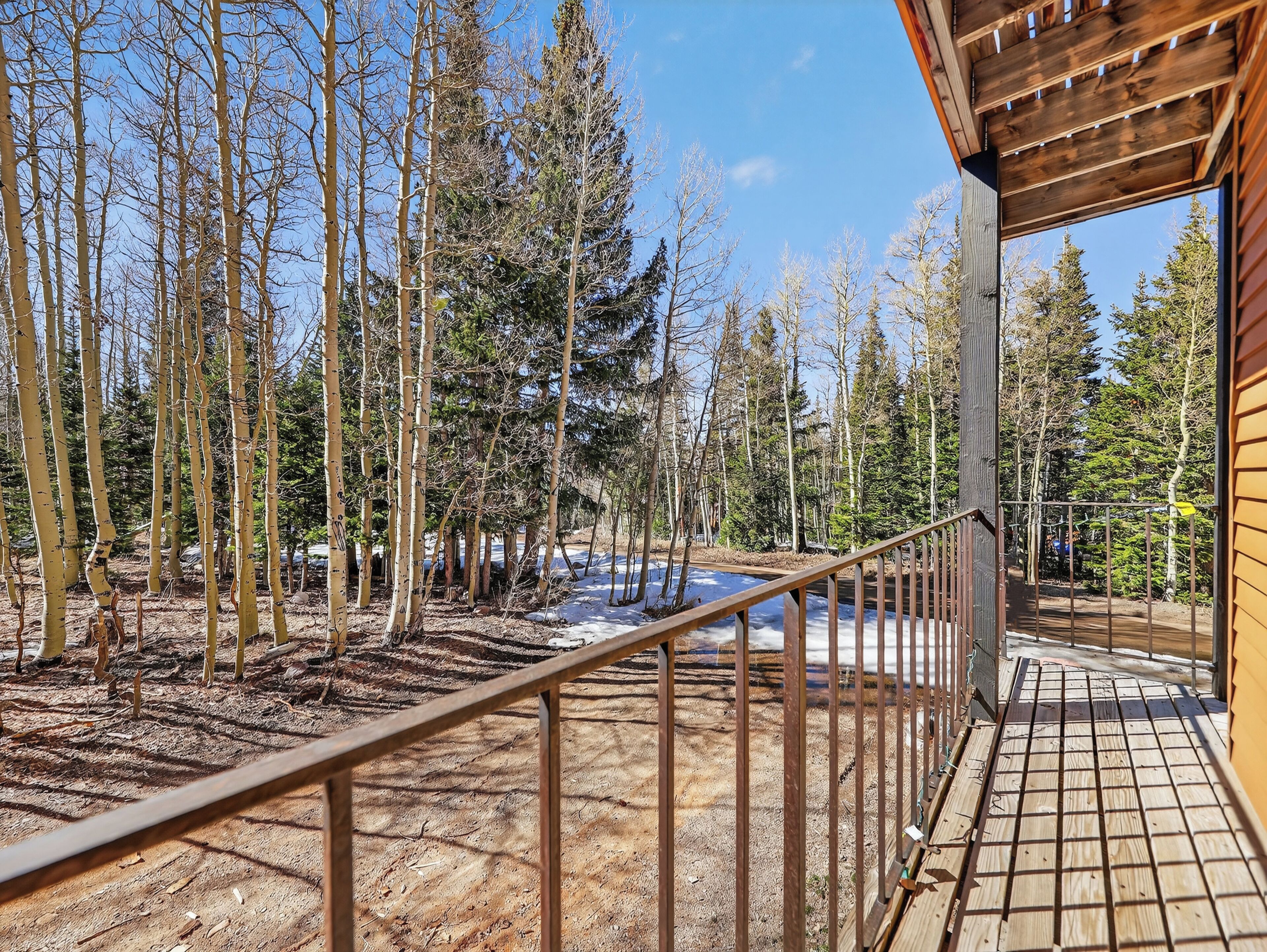 A wooden deck with a metal railing overlooking a forested area with snow on the ground.