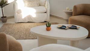 Een moderne woonkamer met een witte bank, een ronde salontafel met een cactus en decoratieve borden, een potplant en een beige vloerkleed.