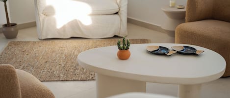 Una sala de estar moderna con un sofá blanco, una mesa de centro redonda con un cactus y platos decorativos, una planta en maceta y una alfombra beige.