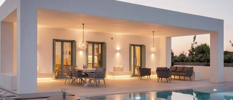 A modern outdoor pool area with a dining setup, lounge chairs, and a clear view of the pool.