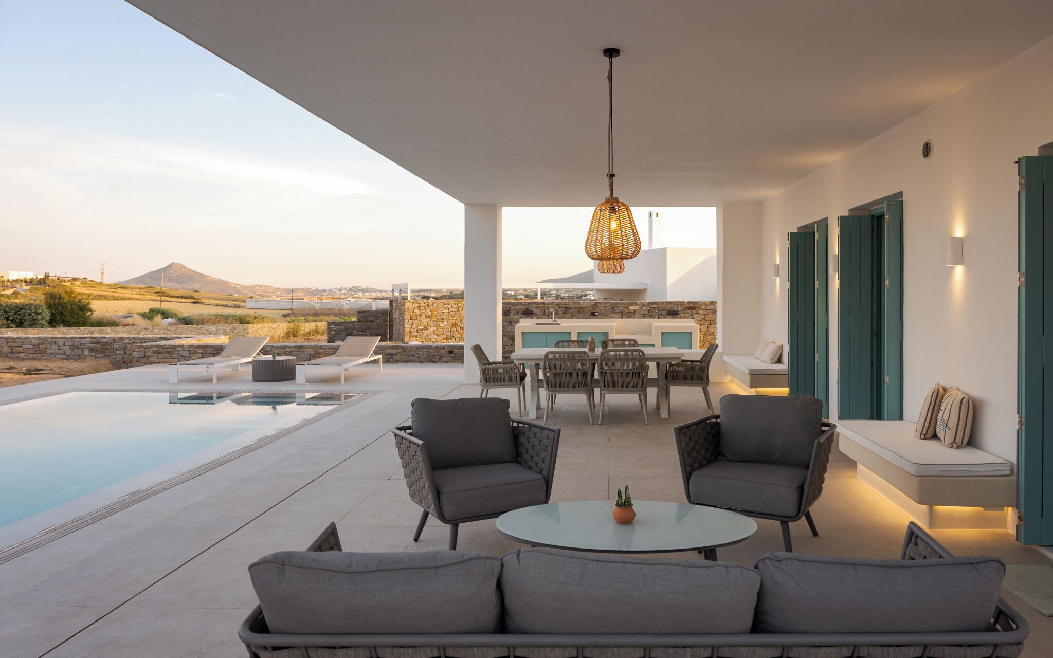 A modern outdoor living area with a pool, lounge chairs, a dining table, and a hanging light fixture.