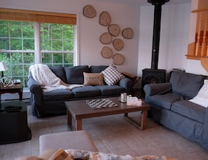 A cozy living room with a fireplace, a sofa, a coffee table, and a window with a view of greenery.