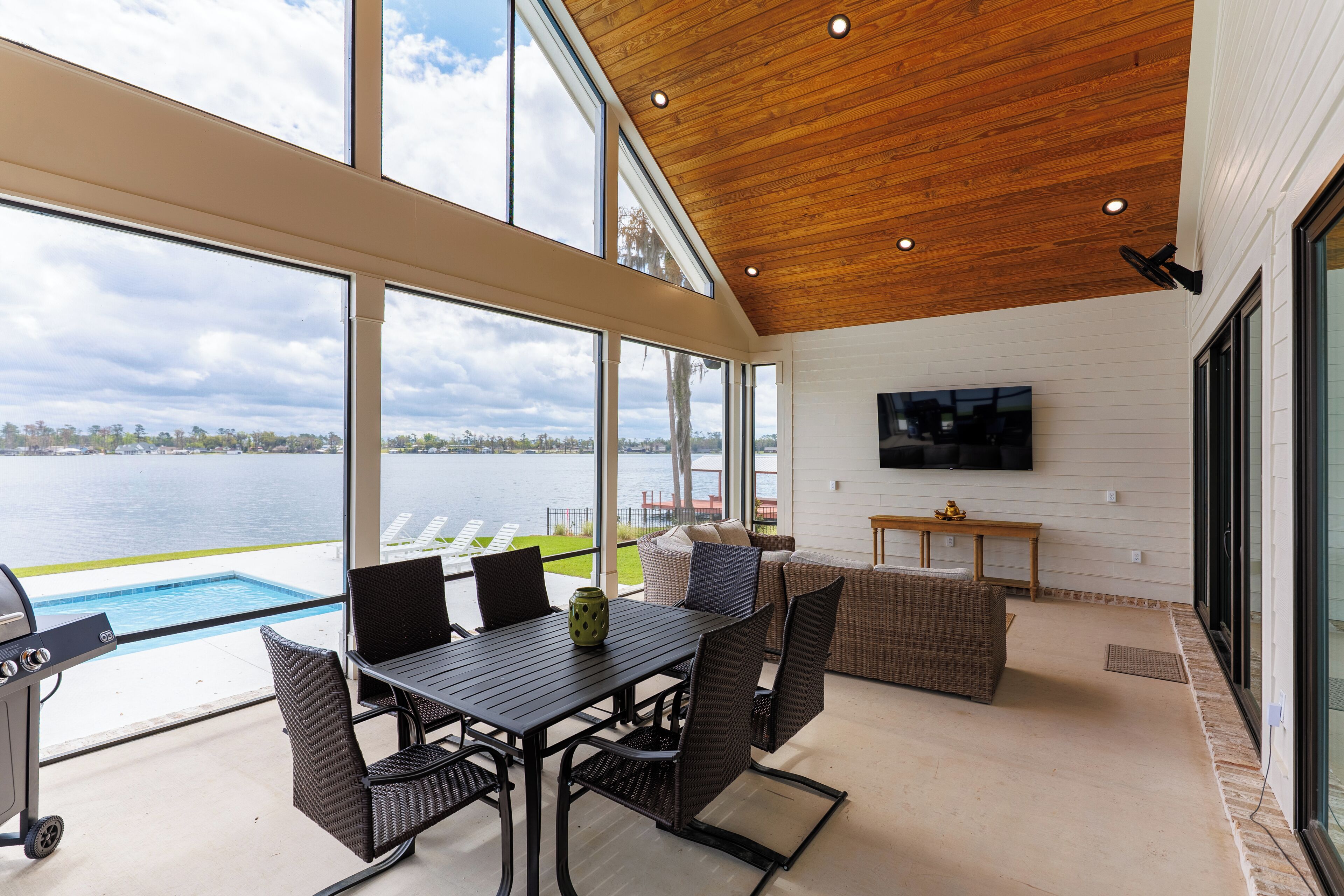 Une vaste terrasse offrant une vue sur un lac, une piscine et un coin repas aménagé avec des meubles en osier.