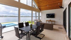Une vaste terrasse offrant une vue sur un lac, une piscine et un coin repas aménagé avec des meubles en osier.