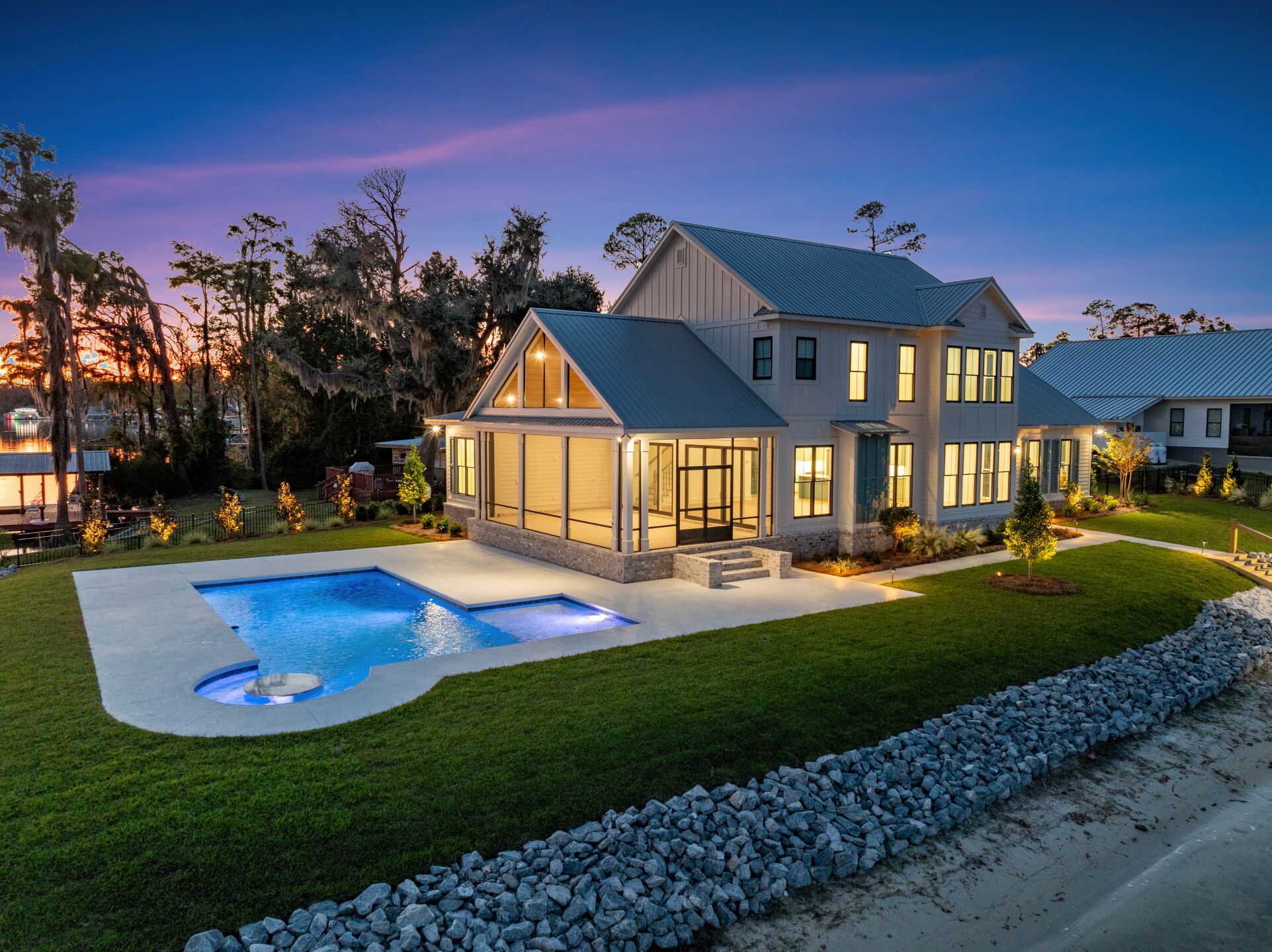 Une maison moderne à deux étages avec une piscine, entourée d’une pelouse bien entretenue et d’une bordure en pierre.