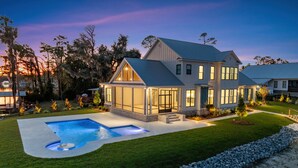 Une maison moderne à deux étages avec une piscine, entourée d’une pelouse bien entretenue et d’une bordure en pierre.