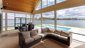 Un salon moderne doté d’un grand canapé d’angle, d’une table à manger avec des chaises, et offrant une vue sur un lac grâce à de grandes fenêtres.