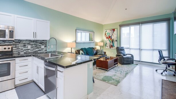 Una cucina moderna con elettrodomestici integrati, una zona pranzo con tavolo e sedie e un soggiorno con divano e una grande finestra.