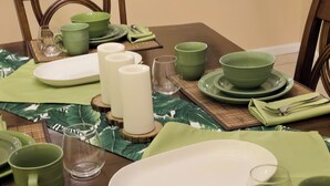 A dining table set with green plates, bowls, and cups, arranged on a woven placemat. - Disney 10 mins private house privacy screen pool, gated community no resort fees (Kissimmee)