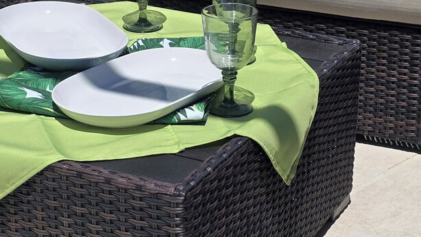 A wicker outdoor seating area with a green tablecloth, a cushion with a leaf pattern, and two white plates and glasses. - Disney 10 mins private house privacy screen pool, gated community no resort fees (Kissimmee)