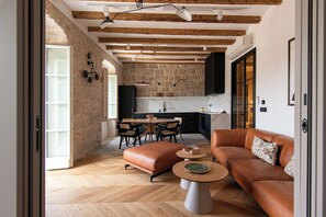 A modern living room with a brown leather sofa, a coffee table, and a dining area with a stone wall and wooden beams. - Santa Croce Suite by DuHomes (Dubrovnik)
