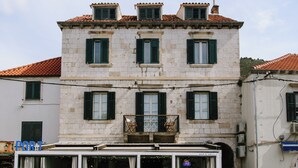 A two-story building with a stone facade, multiple windows with shutters, and a balcony with a metal railing. - Santa Croce Suite by DuHomes (Dubrovnik)