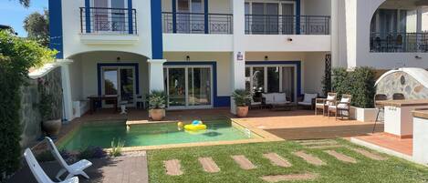 A two-story building with a swimming pool, outdoor seating, and a stone wall.