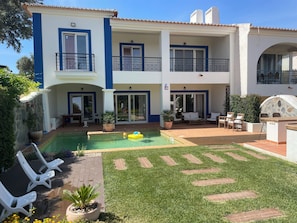 Un edificio de dos plantas con piscina, mobiliario exterior y una pared de piedra.