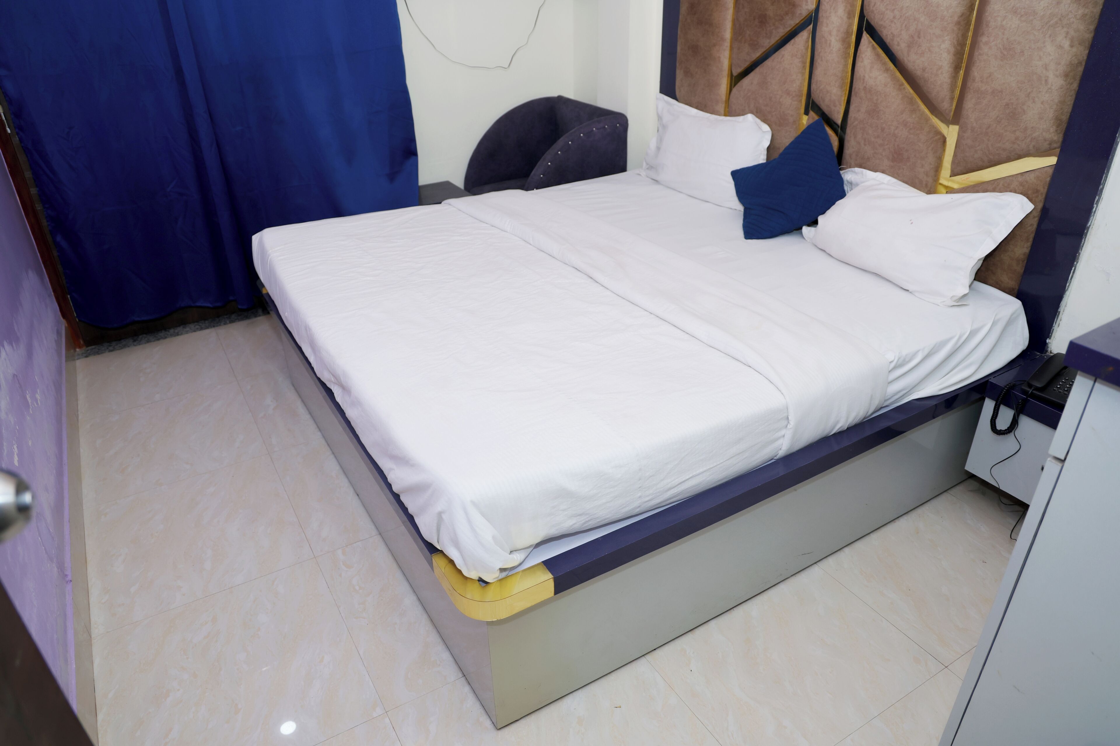 Una cama con ropa de cama blanca, un cabecero con diseños geométricos y una mesita de noche con un teléfono.