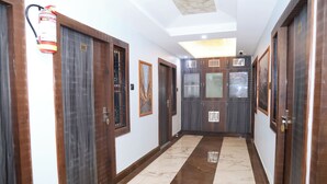 A hallway with wooden doors, a fire extinguisher, and a marble floor. - Pragati Guest House (Gorakhpur)