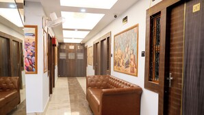 A hallway with a brown leather sofa, wooden doors, and a ceiling fan. - Pragati Guest House (Gorakhpur)