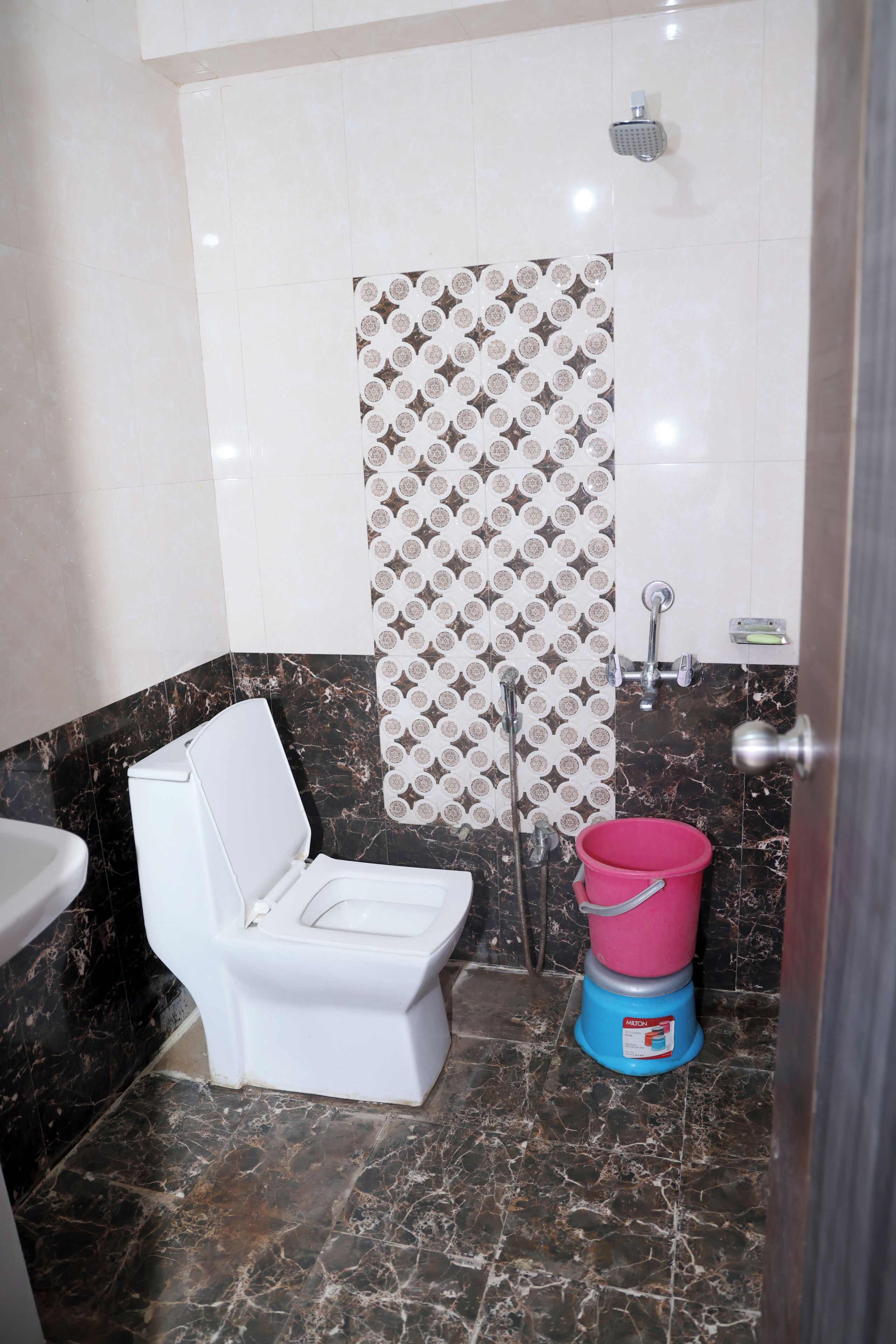A bathroom with a toilet, a shower, and a bucket.