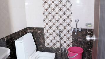 A bathroom with a toilet, a shower, and a bucket.