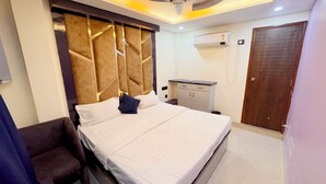 A bedroom with a bed, a desk, an air conditioning unit, and a door. - Pragati Guest House (Gorakhpur)