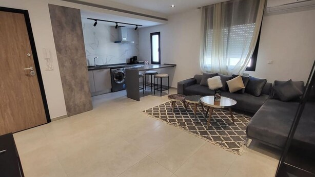 Uma sala de estar moderna com um sofá, mesa de centro e uma área de cozinha com máquina de lavar.