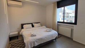 Quarto de hotel moderno com uma cama grande, uma janela com cortinas, um radiador e um ar condicionado fixado na parede.