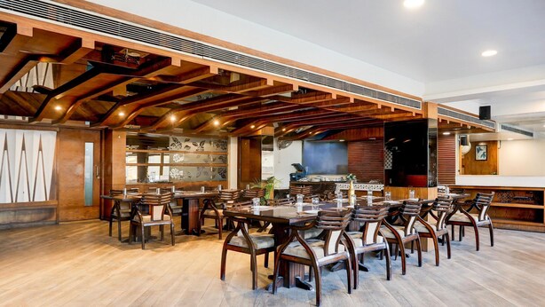 Um restaurante com vigas de madeira, várias mesas e cadeiras.