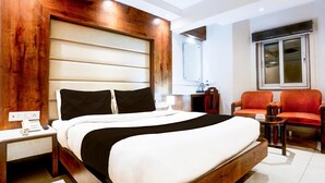 Quarto de hotel com uma cama grande, mesa de cabeceira com telefone, pequena mesa com abajur e duas cadeiras.