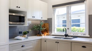 A kitchen with white cabinets, a microwave, a sink, and a window with a view of greenery.