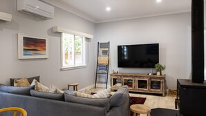 Een woonkamer met een grijze bank, een flatscreen televisie, een houten kast en een raam met uitzicht op groen.