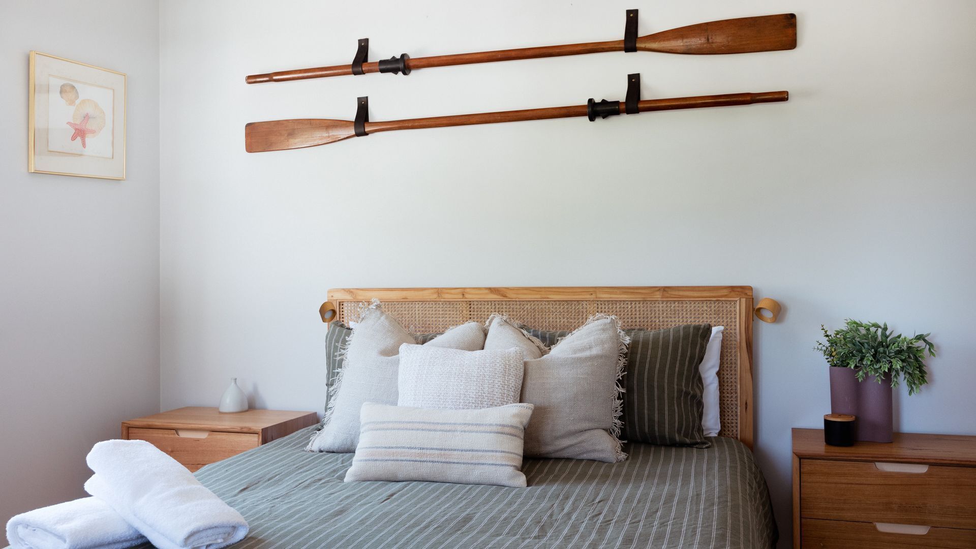 Ein Schlafzimmer mit Bett, Kissen, einem Kopfteil, einem Nachttisch, einem gerahmten Bild und zwei Holzschlägern an der Wand.