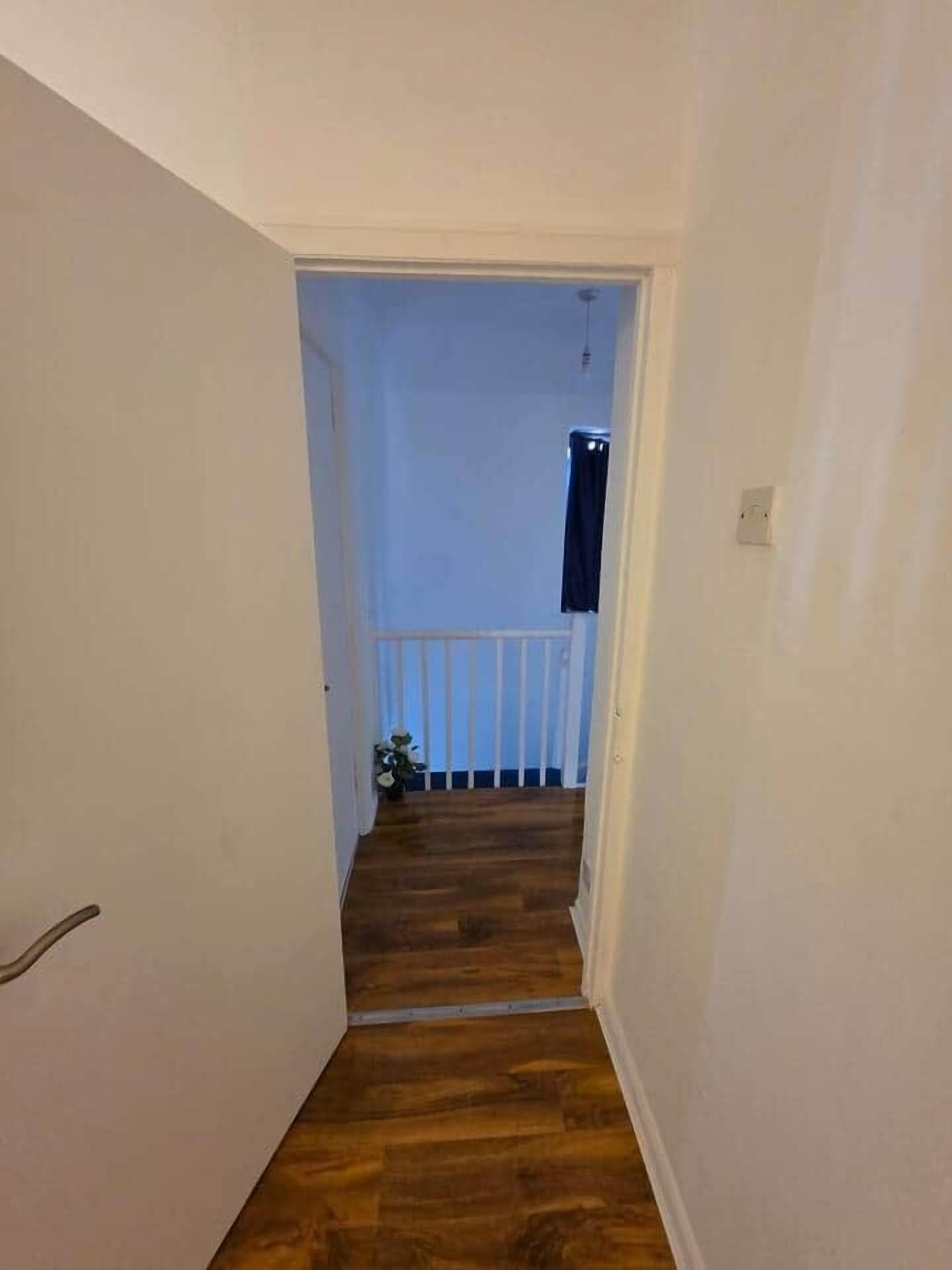 A narrow hallway with wooden flooring leading to a balcony with a white railing.