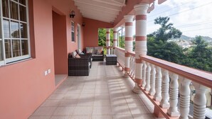 Ein überdachter Balkon mit Fliesenboden, einer Sitzecke mit Kissen und einem Geländer mit Zierelementen.