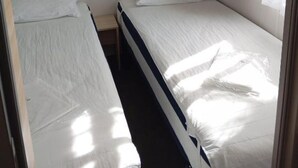 A small, single-bed room with a bed, a nightstand, a wall-mounted light, and a window with curtains. - 🌞 Rent Mobil-Home all comfort - Near Lac de Sainte-Croix 🌿 (Sainte-Croix-du-Verdon)